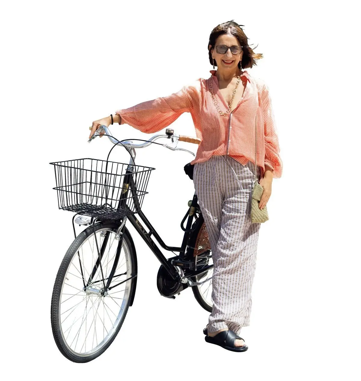 赤い縁取りの眼鏡をかけた女性が、黒い自転車のハンドルに手を添え、笑顔で立っている。女性は、ピンクと白のストライプのシャツと、グレーのストライプのパンツ、黒いサンダルを着用。自転車には黒いカゴが付いている。