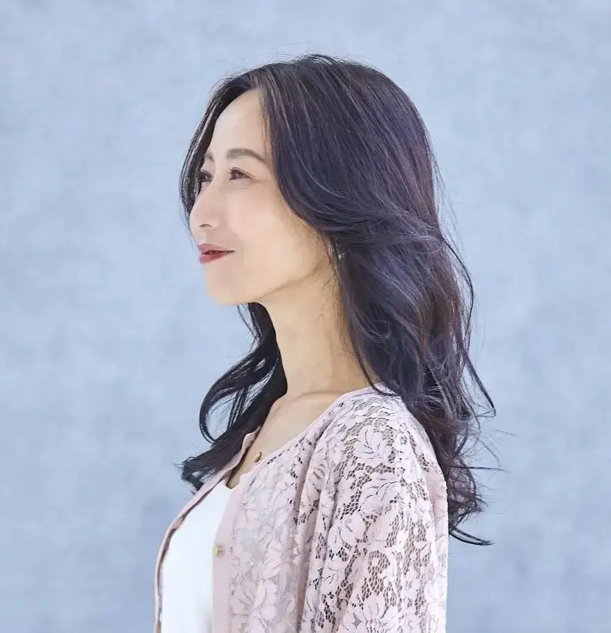 左を向いた女性で、波打った黒い髪が肩まで落ち、淡いピンクのレースカーディガン姿。