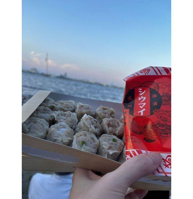 夕暮れ時の海を背景に、白い容器に入った肉まんが並んでいる。右には辛ラーメンの赤いパッケージが握られている。