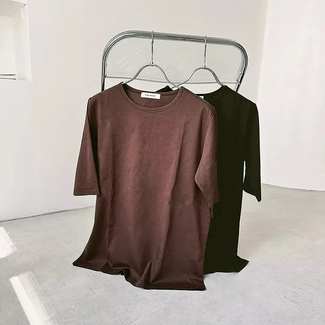 茶色の長袖Tシャツと黒の長袖トップスがハンガーにかけられ、簡素な部屋に展示されている
