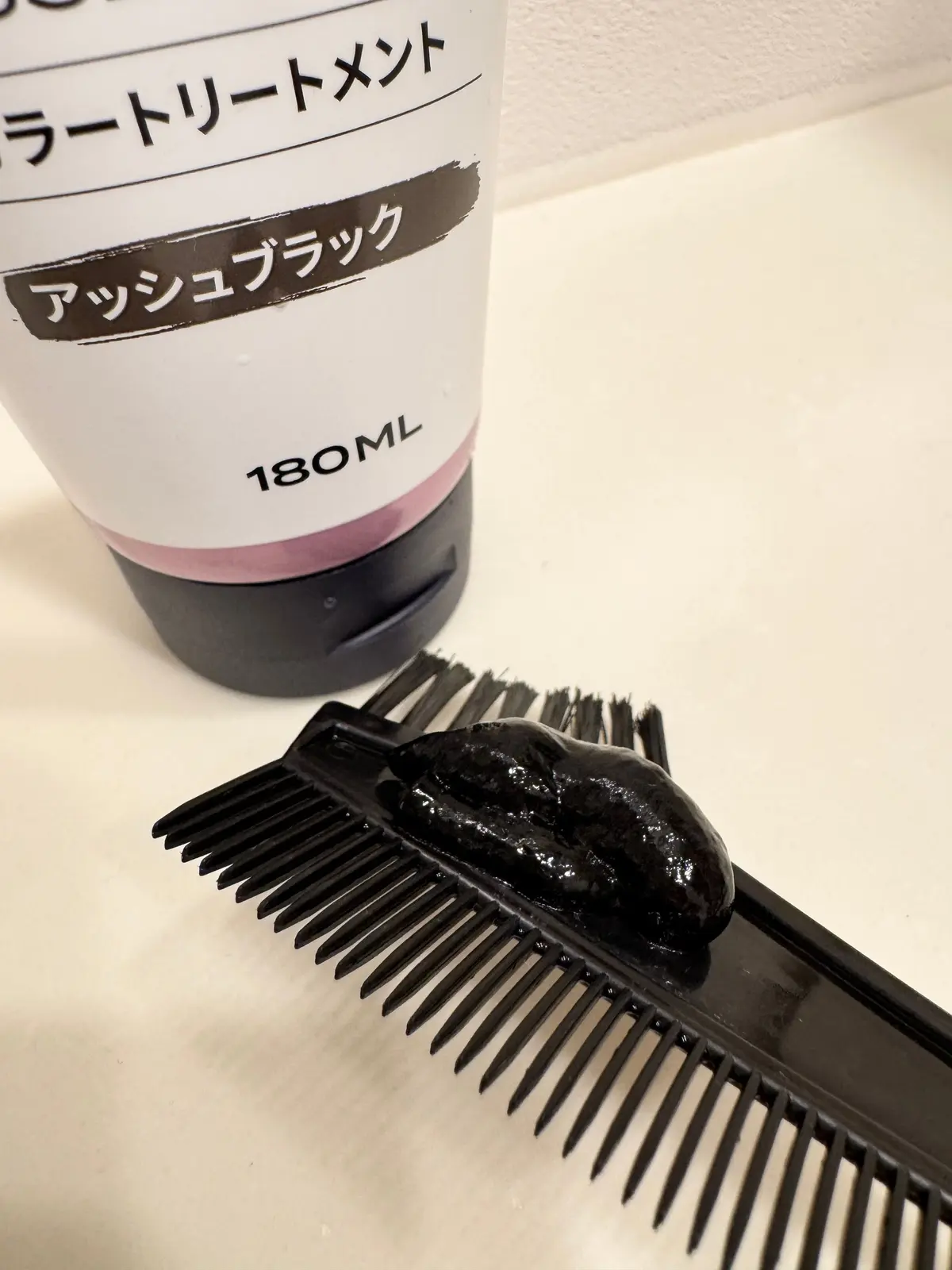 白とピンクのチューブに入った「アッシュブラック」と書かれたヘアクリーム。クリームを塗った黒い櫛がチューブの横に置かれている。容量は180ml。