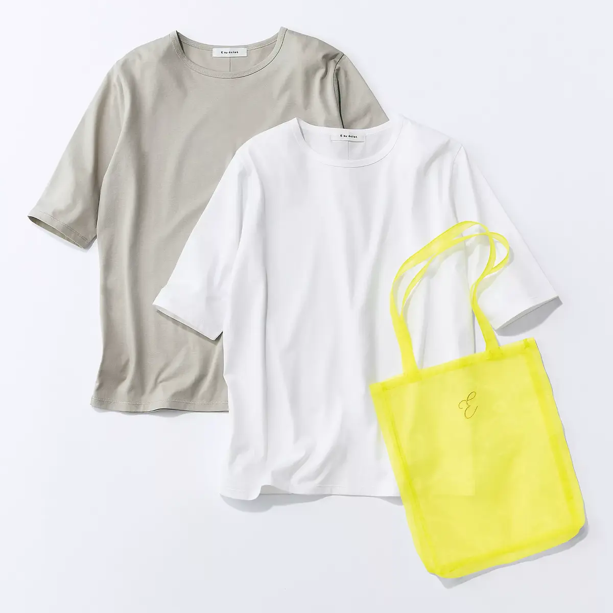 白とグレーのクルーネックTシャツ2枚と、ネオンイエローのトートバッグが置かれている様子。Tシャツは畳まれ、バッグはひっくり返った状態で配置されている。