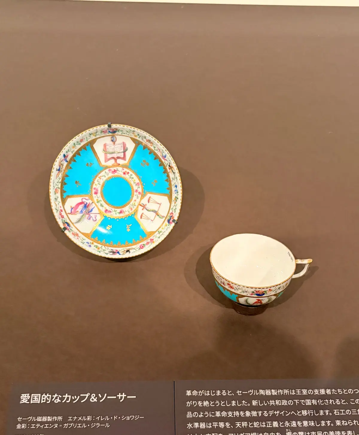 セーブル陶器製所のカップとソーサー。淡いピンクの地に、鮮やかな色使いで花鳥風物の絵が描かれ、金彩が施されている。ソーサーも同様のデザイン。