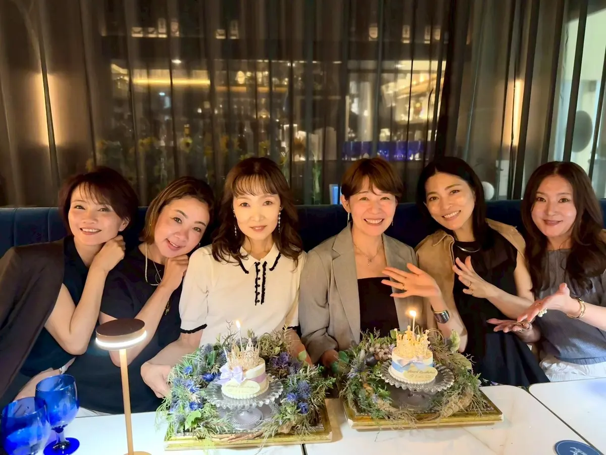 梅田ブルーバードでの誕生日ディナー女子会の集合写真 　6人の女性がテーブルに座り、2つの小さなケーキと花飾りがあり、ろうそくが点っている。