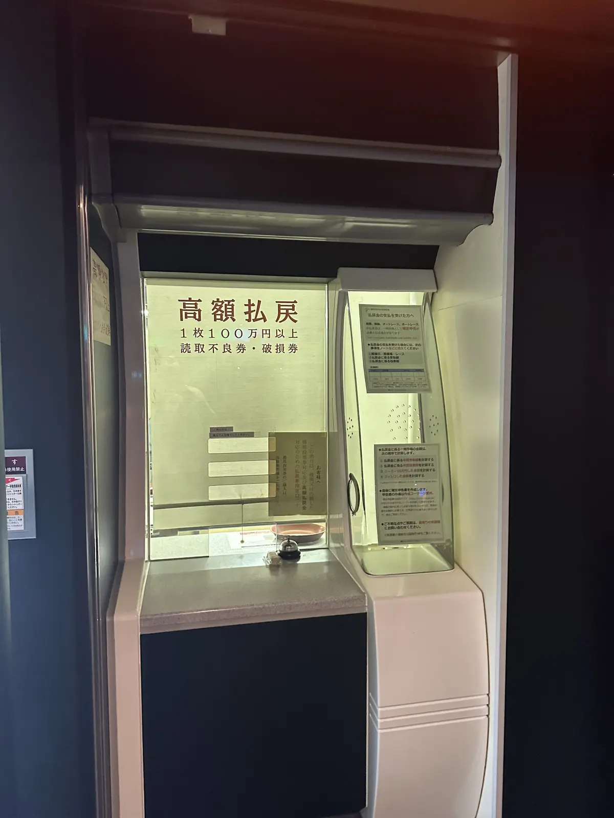 銀行の高額紙幣両替機。窓口には「高額払戻」の文字と、100万円以上の紙幣は取り扱えない旨の注意書きが赤い文字で表示されている。窓内には金属製の仕切りがある。