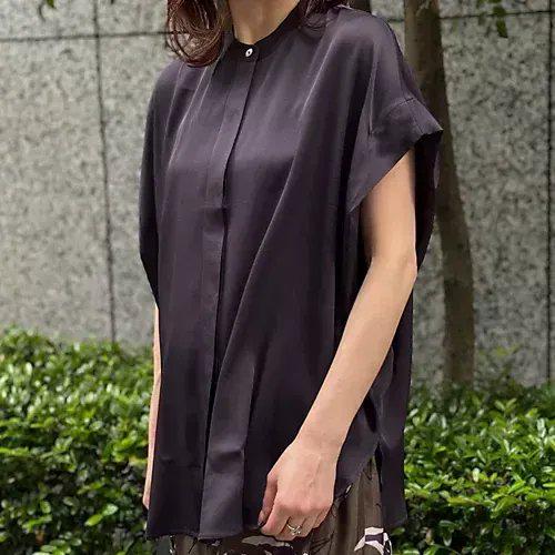 黒いサテン素材のシャツ。前合わせはボタンで、胸に縦のプリーツが入る。袖は短いカフス付きで、肩から袖にかけて切り替えのデザイン。ゆったりとしたシルエット。