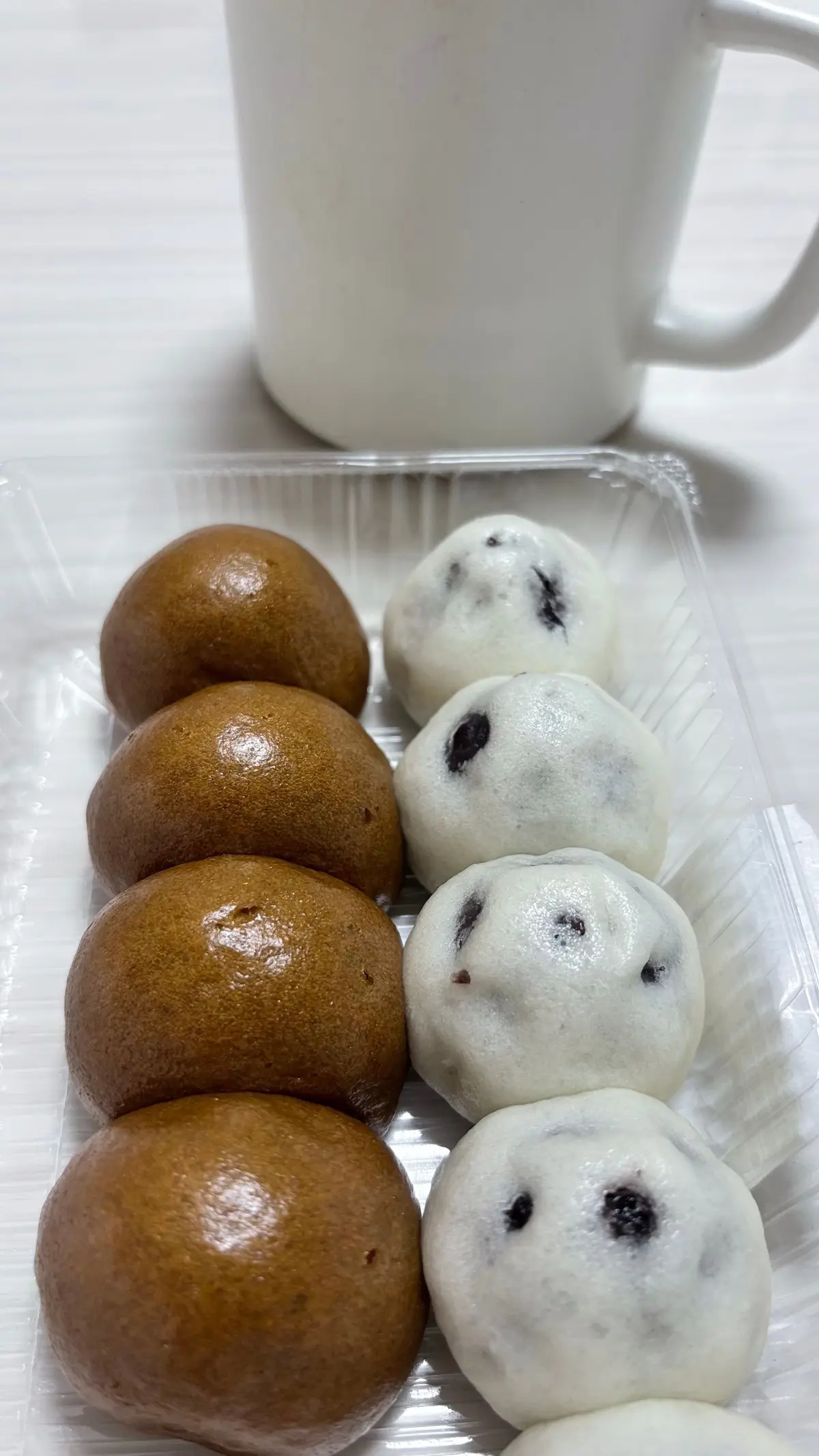 プラスチックトレイに茶色と白の二色のお餅が並んでいる。茶色のお餅が四つ、白のお餅が六つあり、白のお餅には黒いぶつぶつが入っている。