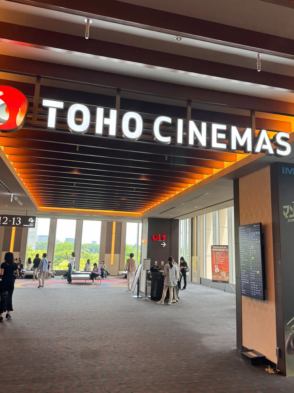 TOHO CINEMASのロビーは天井が木製で明るく、映画のスケジュールが掲げられ、人々が歩き、座っている。