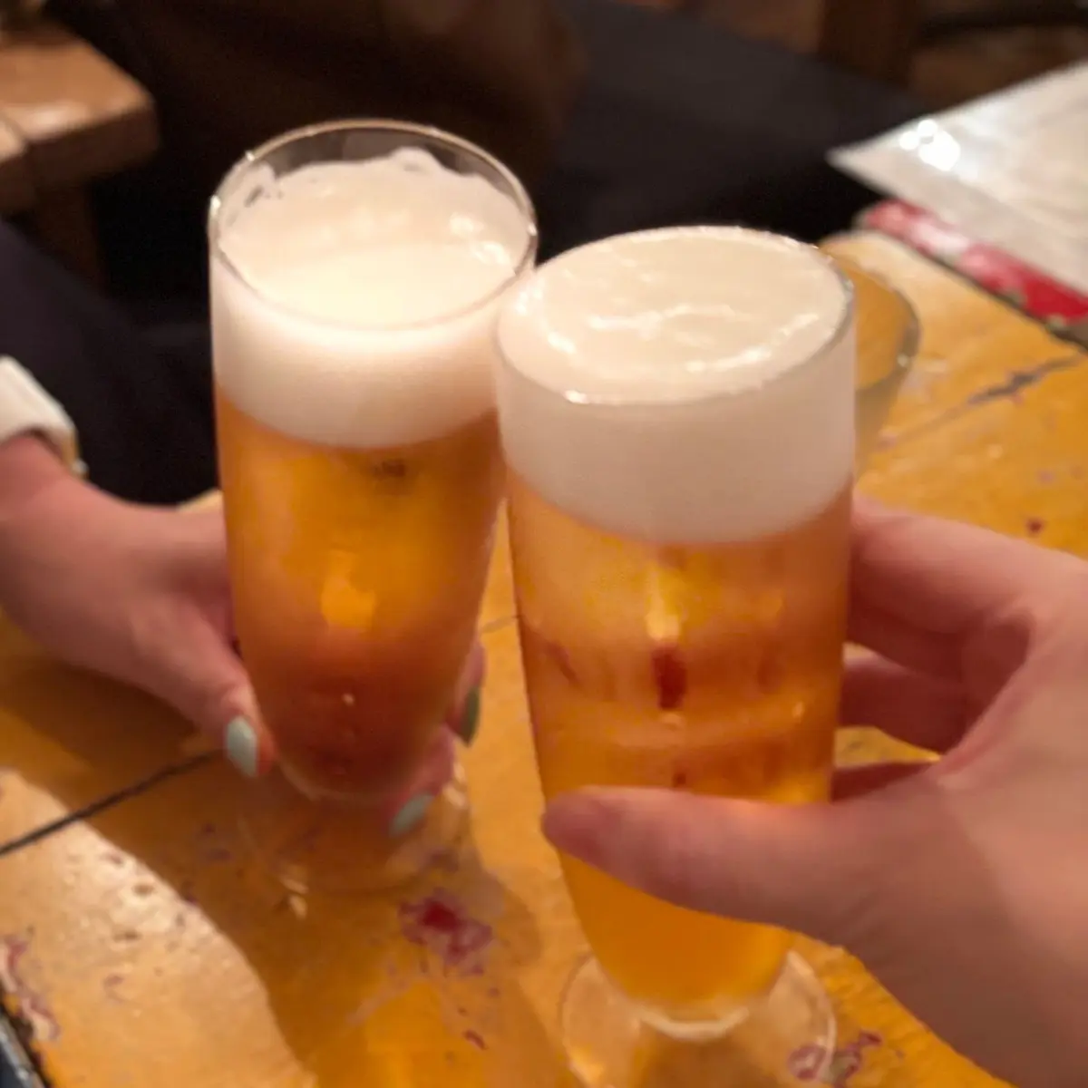 2つのグラスに入った、泡が乗った生ビールが置かれている。手でグラスを持ち、乾杯の様子。