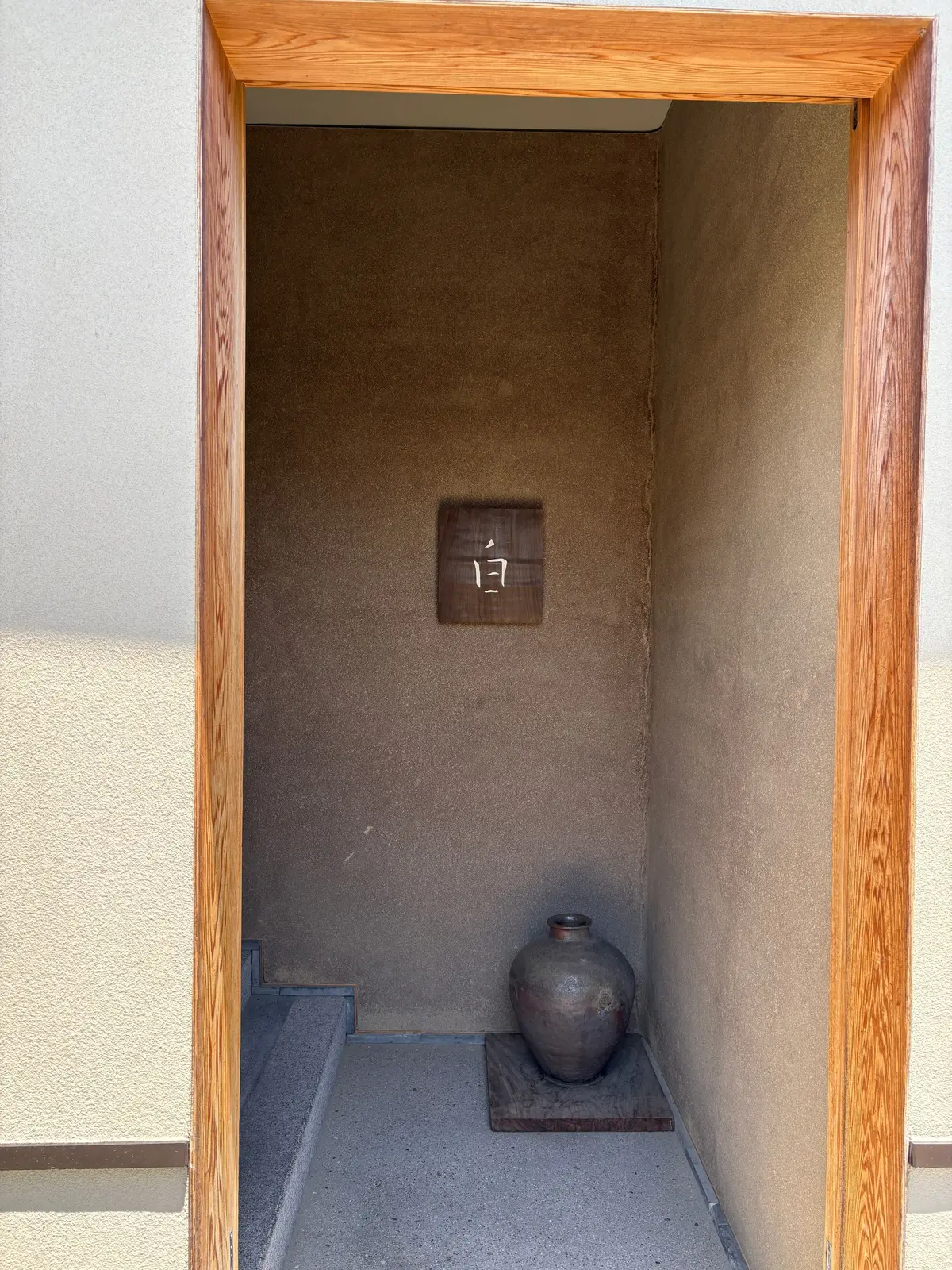 木製の扉から見える狭い部屋で、壁に「17」の看板があり、土製の壺が木製の台に置かれている
