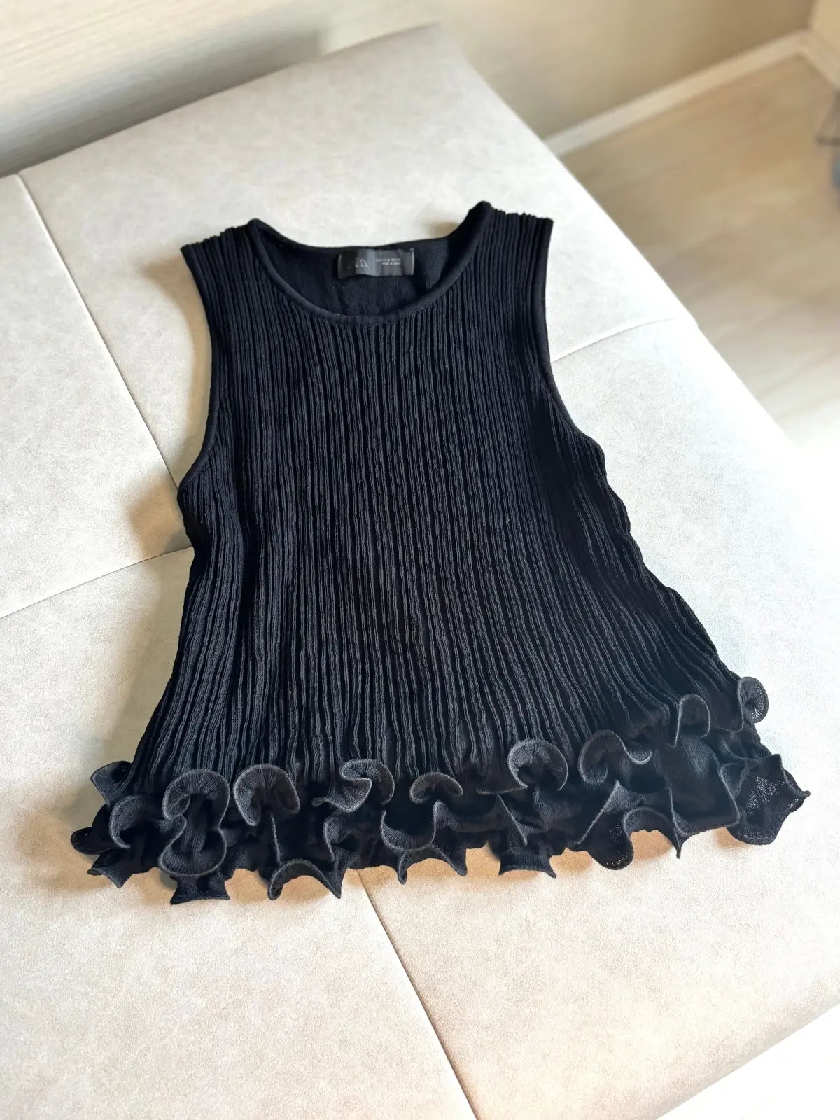 黒色のノースリーブトップス。上部は縦方向にプリーツ加工が施され、裾はフリルがあしらわれている。ZARAのロゴがタグに付いている。