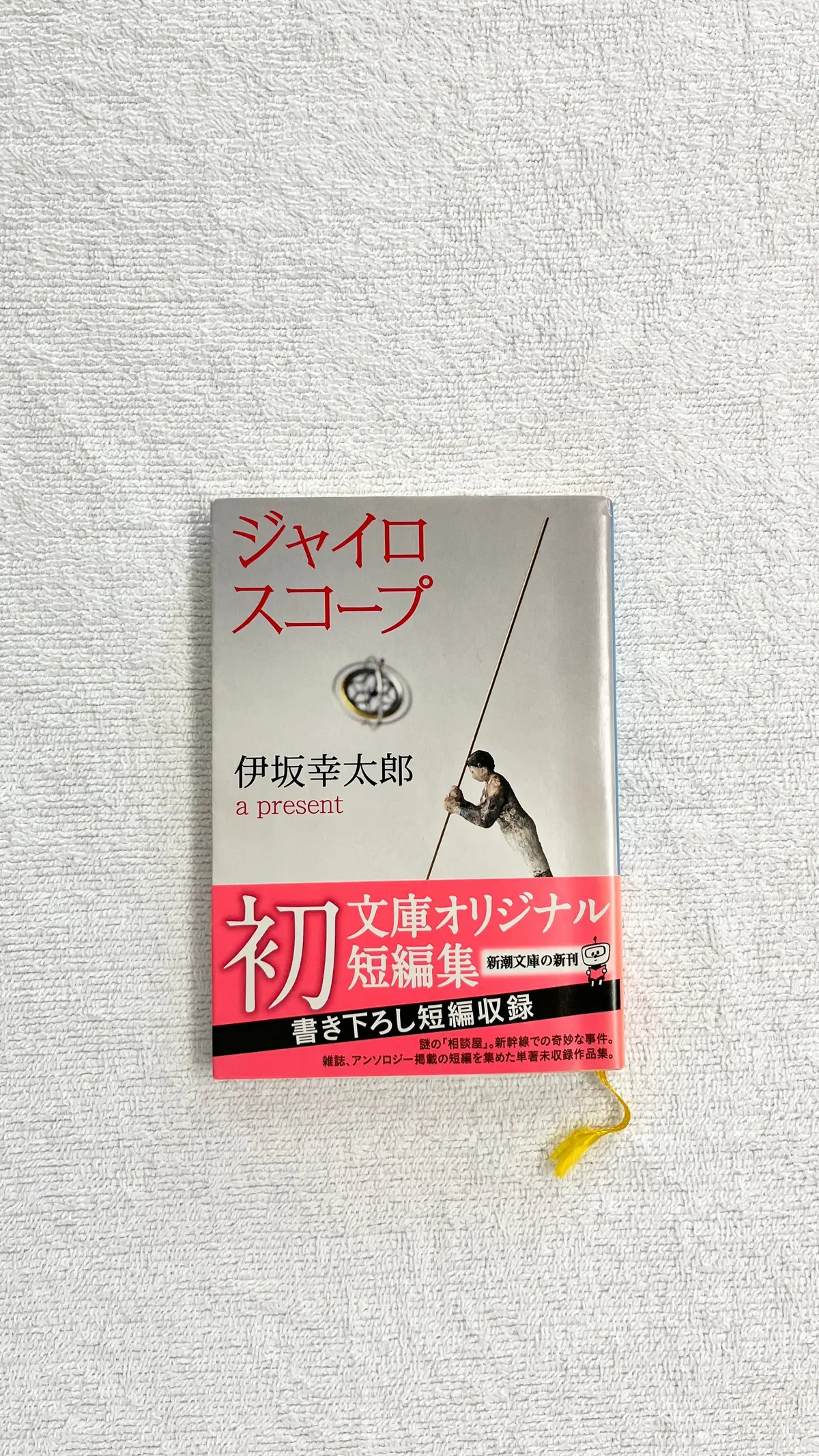 白い背景に置かれた書籍。表紙は黄、赤、白の配色で、中央に男性が釣り糸を持っているイラスト。タイトルは「文庫オリジナル 初 短編集 書き下ろし短編収録」。作者は伊坂幸太郎。