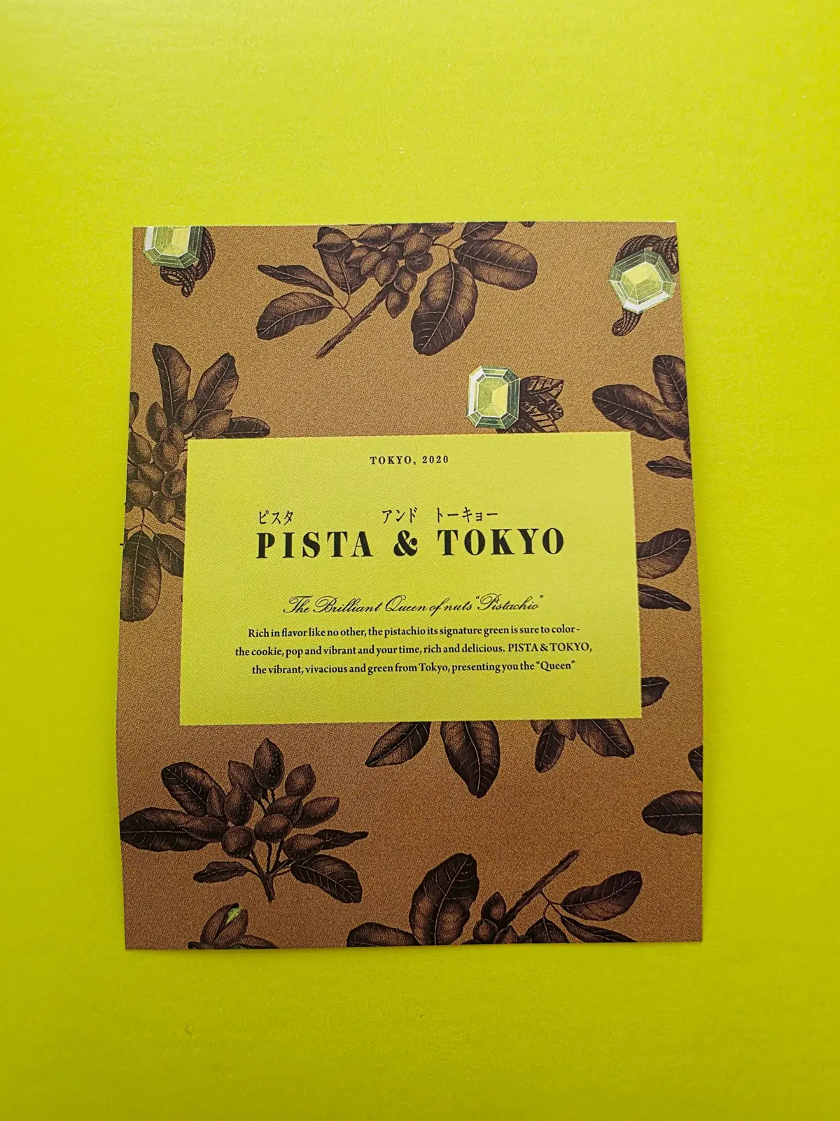 茶色の背景に、ピスタチオのイラストが散りばめられたカード。中央に「PISTA & TOKYO」と記載された黄色のラベルがあり、ピスタチオのフレーバーをアピールするテキストが添えられている。