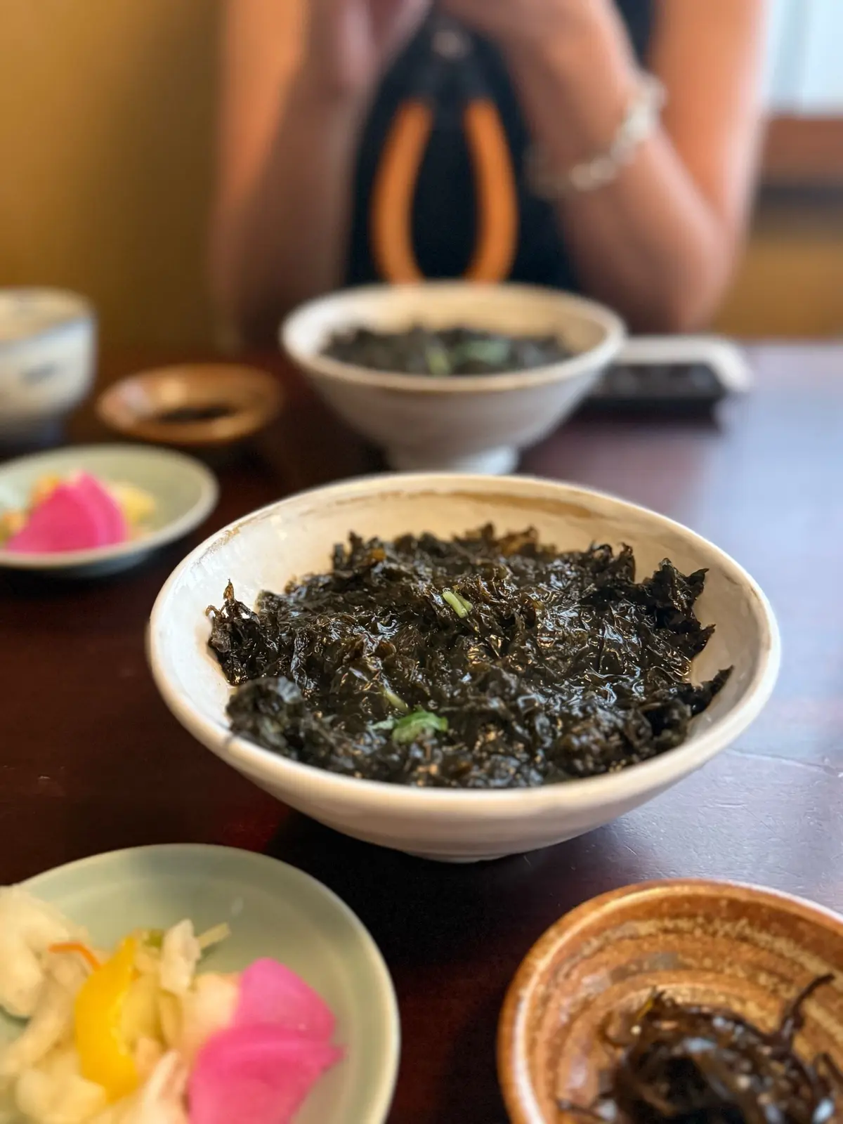 根津、串揚げ「はん亭」、ランチコース、白い陶器の鉢にワカメ風の黒い海藻料理が盛り付けられ、周囲には野菜の副菜や小鉢が並ぶテーブル