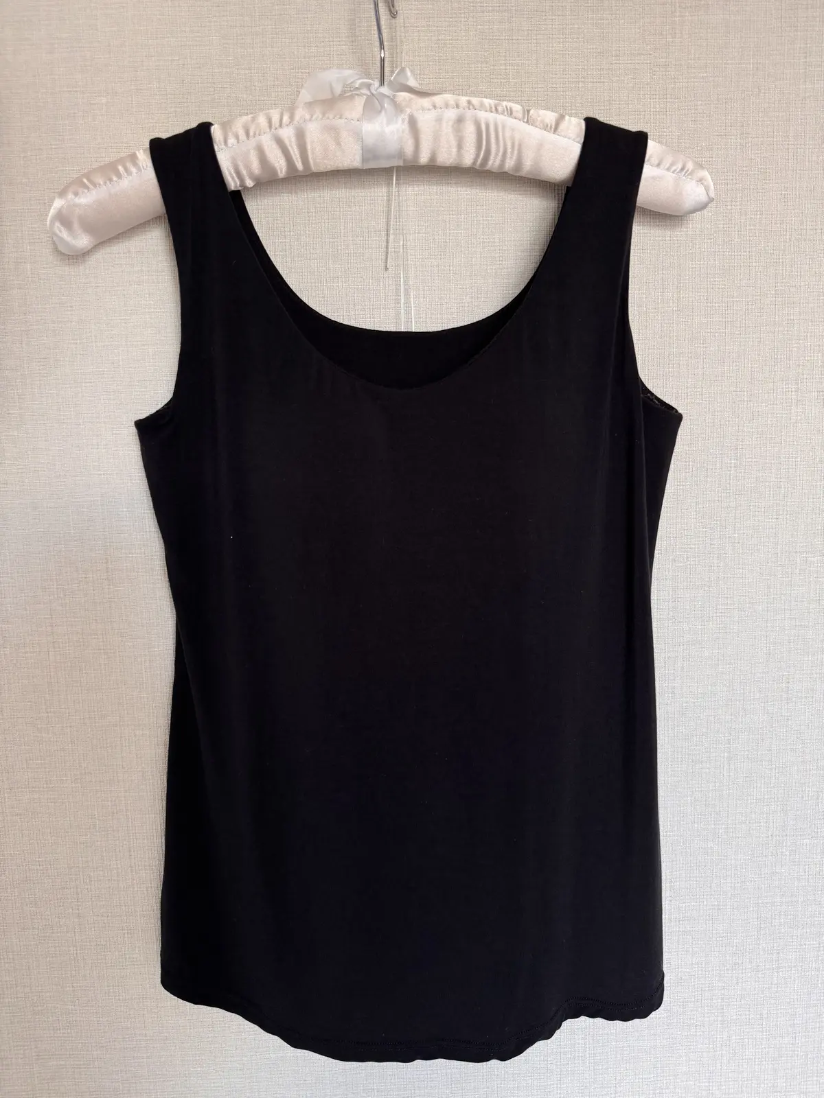 黒いタンクトップがハンガーにかけられている写真。シンプルなデザインで、首元はU字型になっている。生地は伸縮性がありそうな素材。