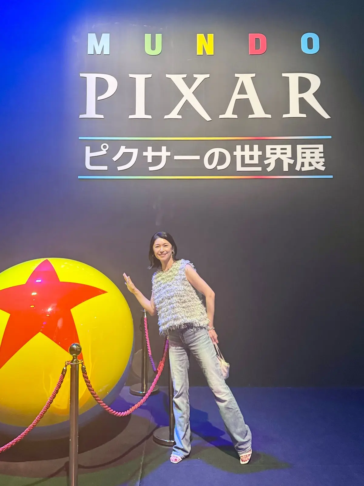 ピクサー展の背景に、黄色いボールと赤い星のオブジェを女性が笑顔でポーズを取っている。背景には「MUNDO PIXAR」の文字。