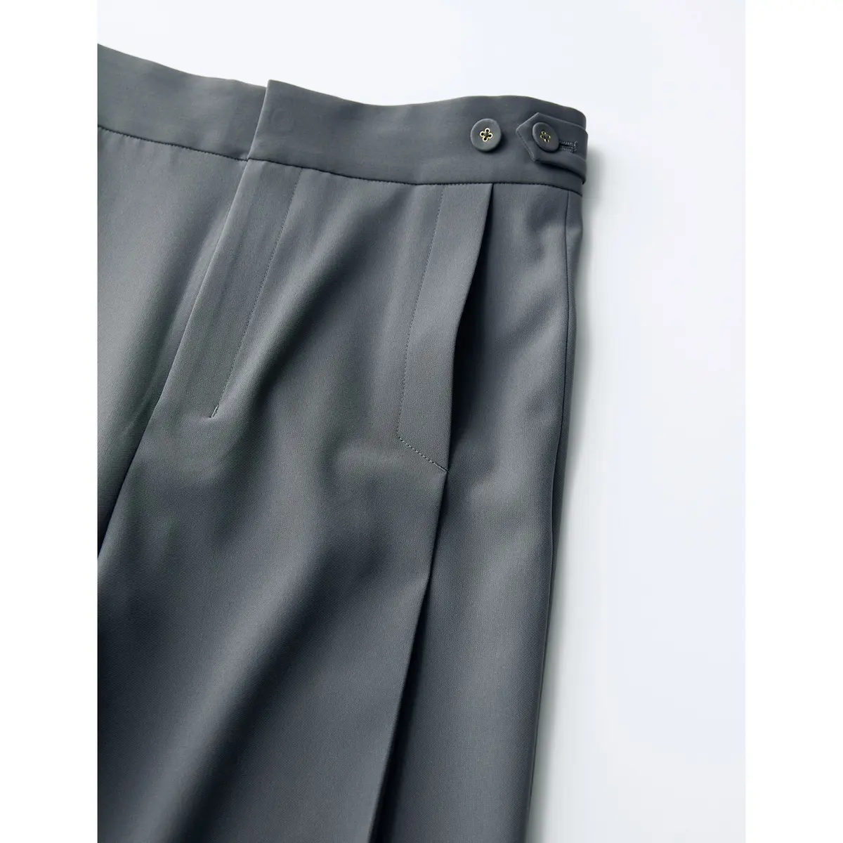 グレーのテーパードパンツ。センタープレスが施され、フロントにボタンが2つ付いている。左側にフラップポケットがある。