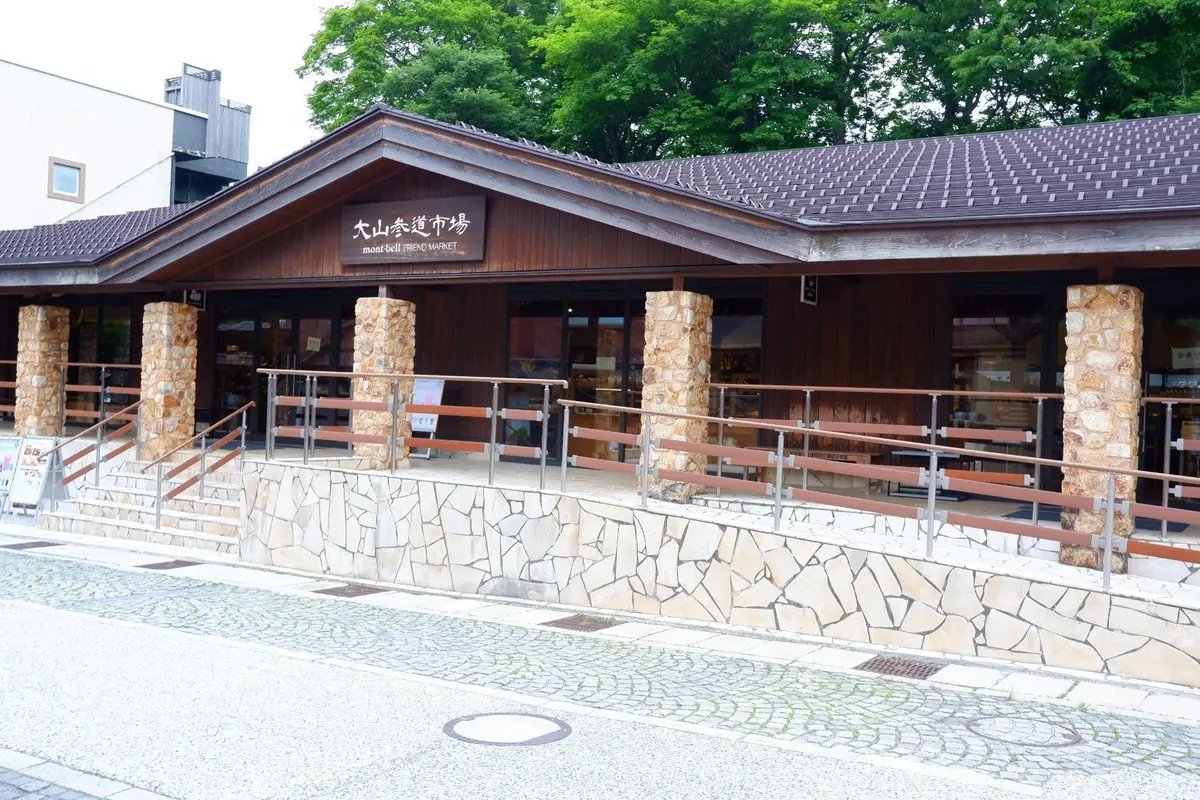木造の建物「モンベルトレンドマーケット」、石造りの柱と手すり付きの段差、緑豊かな木々が背景にある