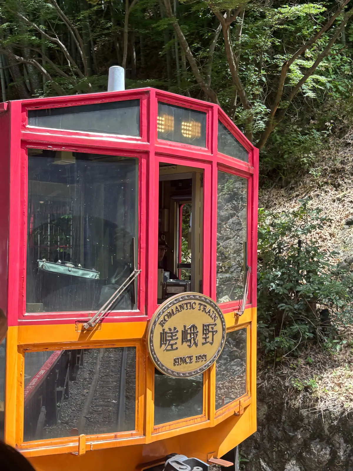 赤とオレンジの車体が特徴的な「ロマンティック鉄道」の車両。窓から緑豊かな自然が見える。車両正面には「Romantic Train」のロゴと「歴峰野」の文字が描かれている。
