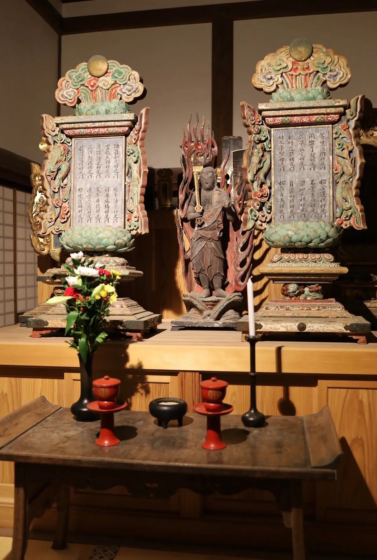 木造の祭壇に、彩色された板碑と不動明王像が安置されている。板碑には漢字で経文が刻まれ、不動明王は炎に囲まれている。祭壇の前には、花瓶や灯籠が置かれている。