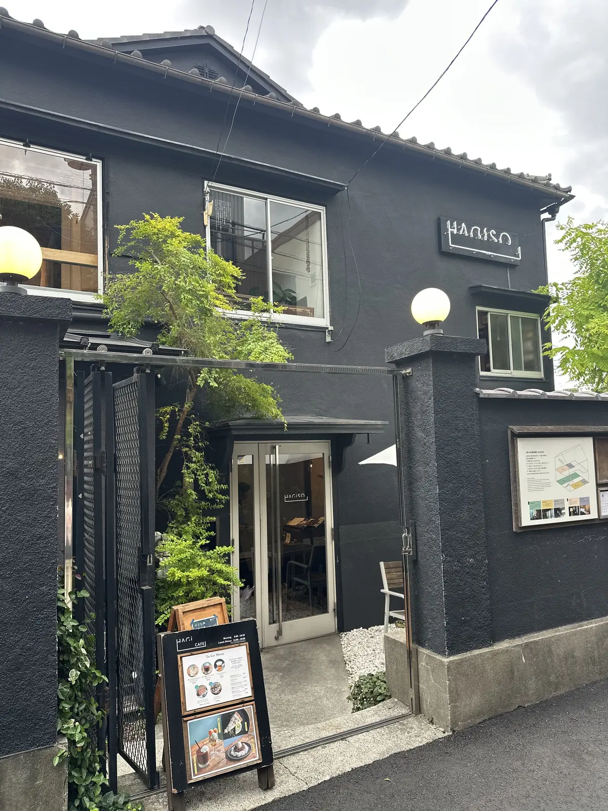黒い外壁の「HARI CAFE」の入り口、ガラス扉とメニュー看板が並ぶ