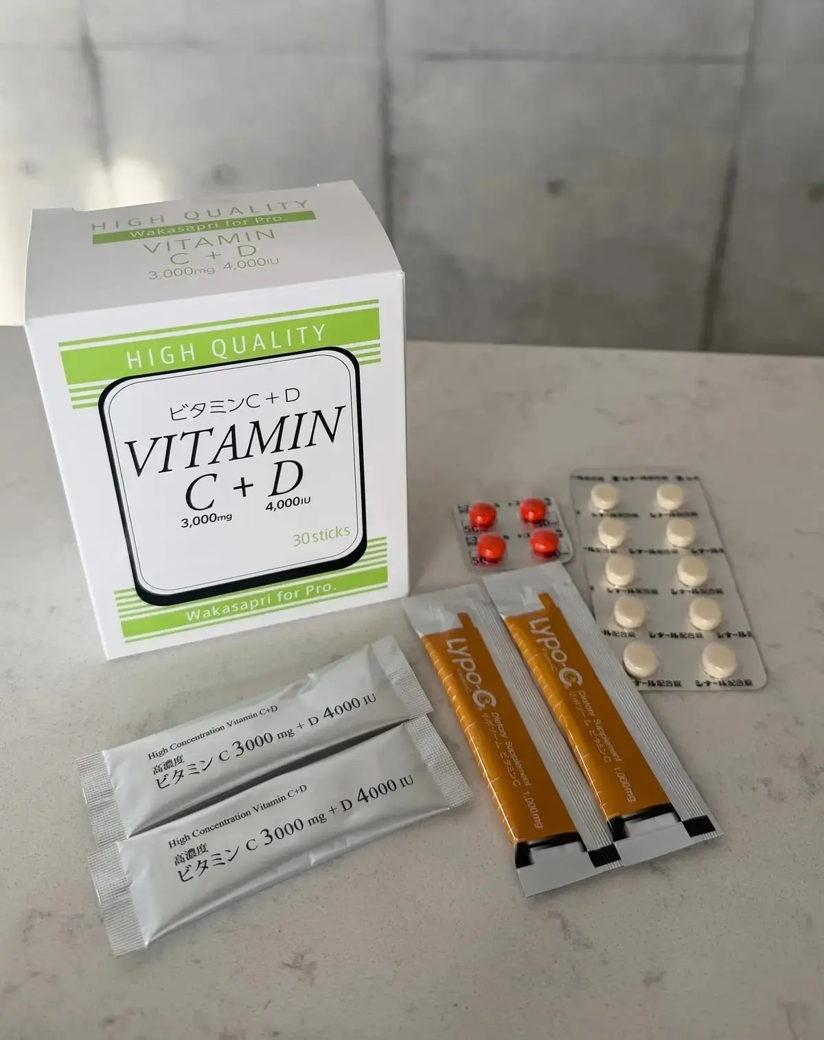 ビタミンC+Dのサプリメント箱と、赤い錠剤と白い錠剤が入った複数の包装が並んでいる