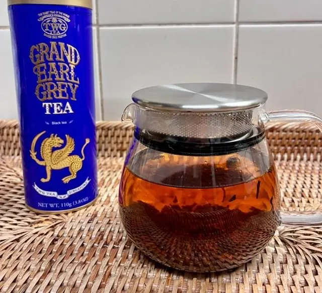 TWGのグランド・アールグレイティーの缶と、茶色のランチョンマットの上に置かれたガラス製のティーポット。ティーポットには茶色の紅茶が淹れてあり、金属製の蓋が乗っている。