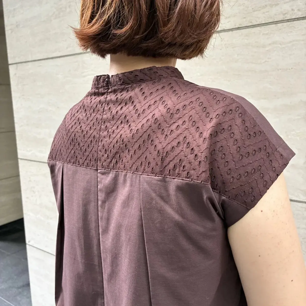 紫がかった茶色のシャツの背面。襟付きで、肩から背中にかけて細かい幾何学模様のテクスチャが入る。袖口にも同様の模様が見られる。