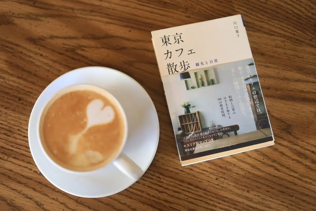 木製テーブルに白いカップにラテアートが乗せられ、右には「東京カフェ改造」の本が置かれている