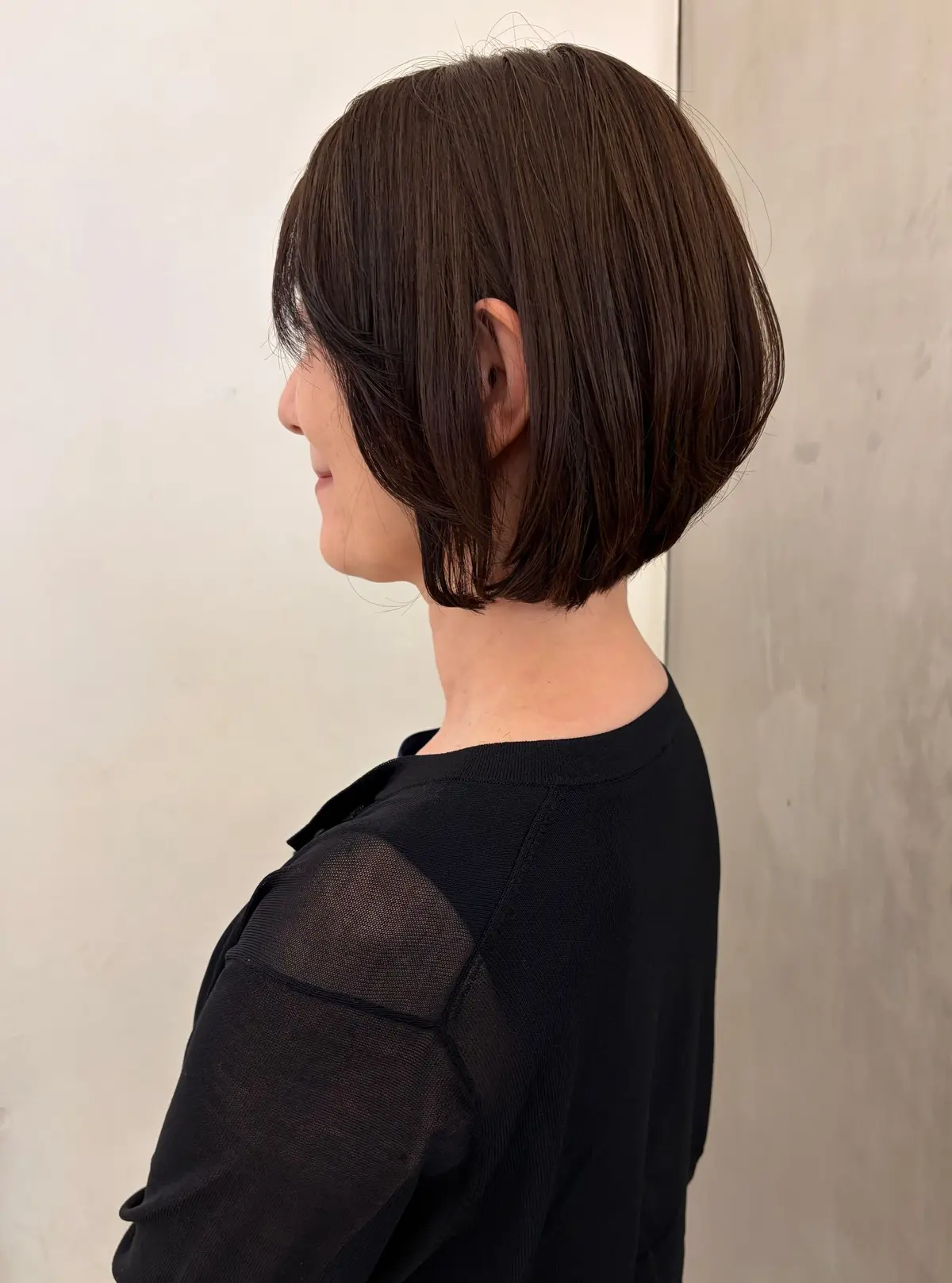 ショートボブの女性が後ろ姿で、左耳と首が見える。黒い透け感のある服を着ている。
