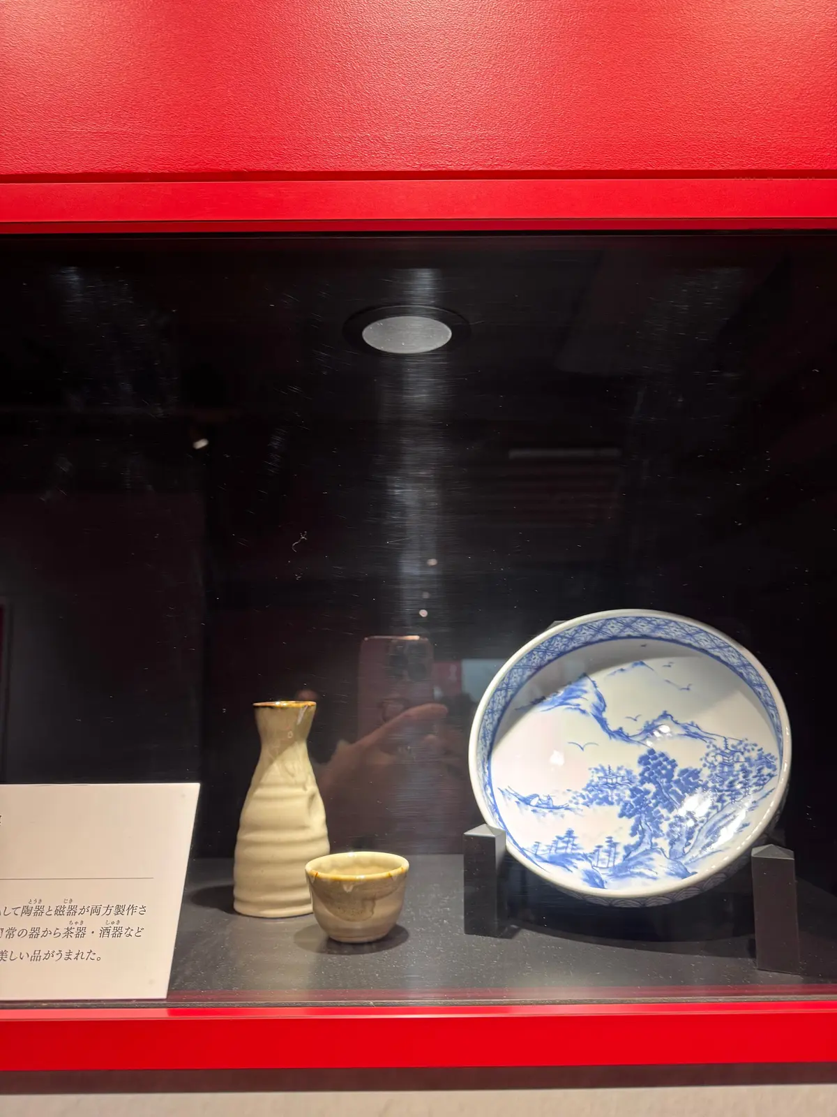 ガラスケースに展示された陶器3点。左から茶色い細長い壺、小さな茶色いカップ、青と白の風景模様が描かれた大きな皿。