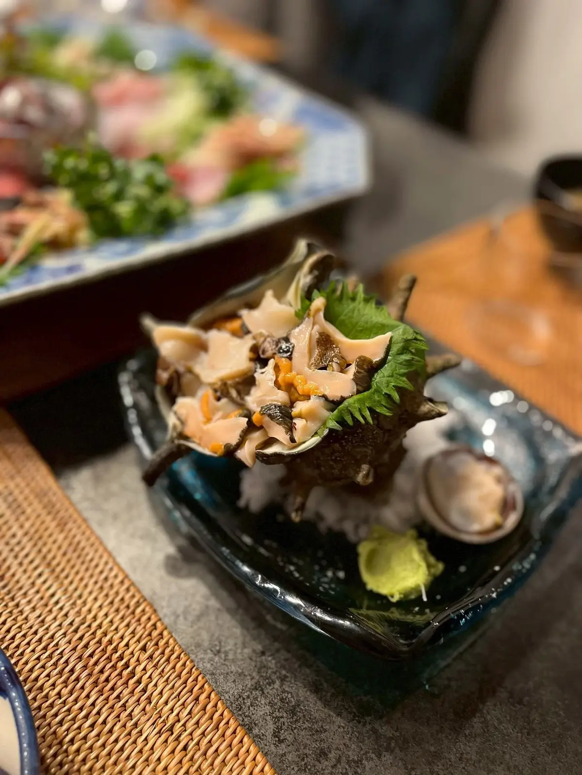 貝類と野菜を盛りつけた黒い料理皿、ワサビと卵黄が添えられた料理