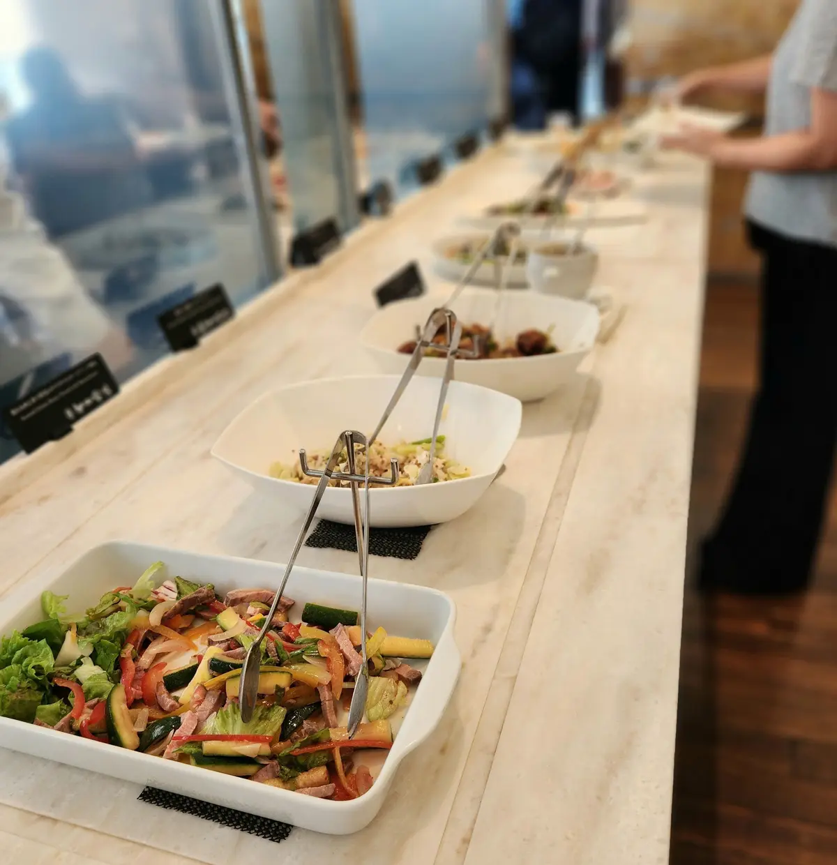 ビュッフェ台に並べられたサラダ、米料理、肉料理のボウルとトレイ、トングが置かれている