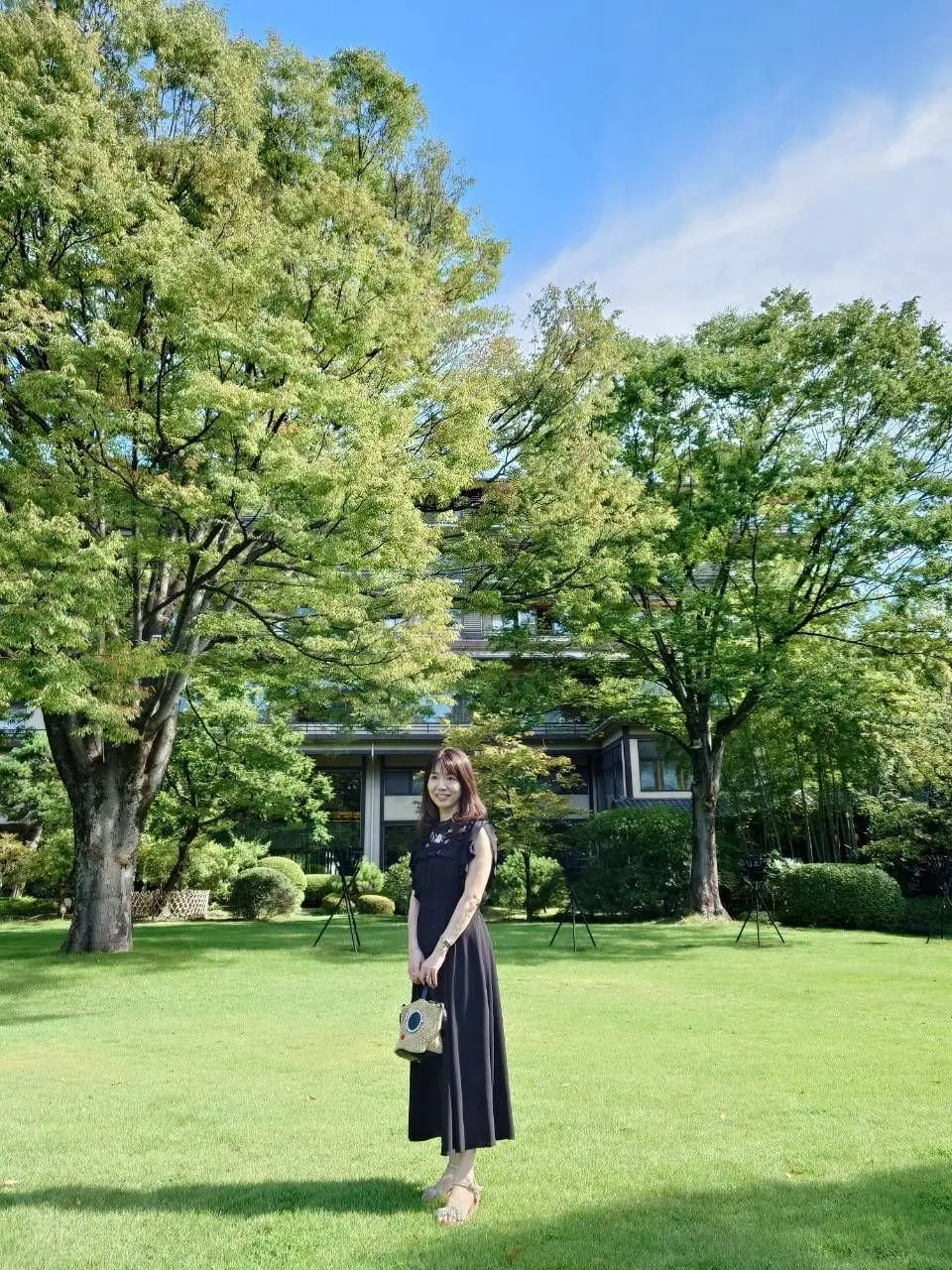 緑の芝生の上で、黒いワンピースを着た女性が立っている。常磐ホテルの日本庭園