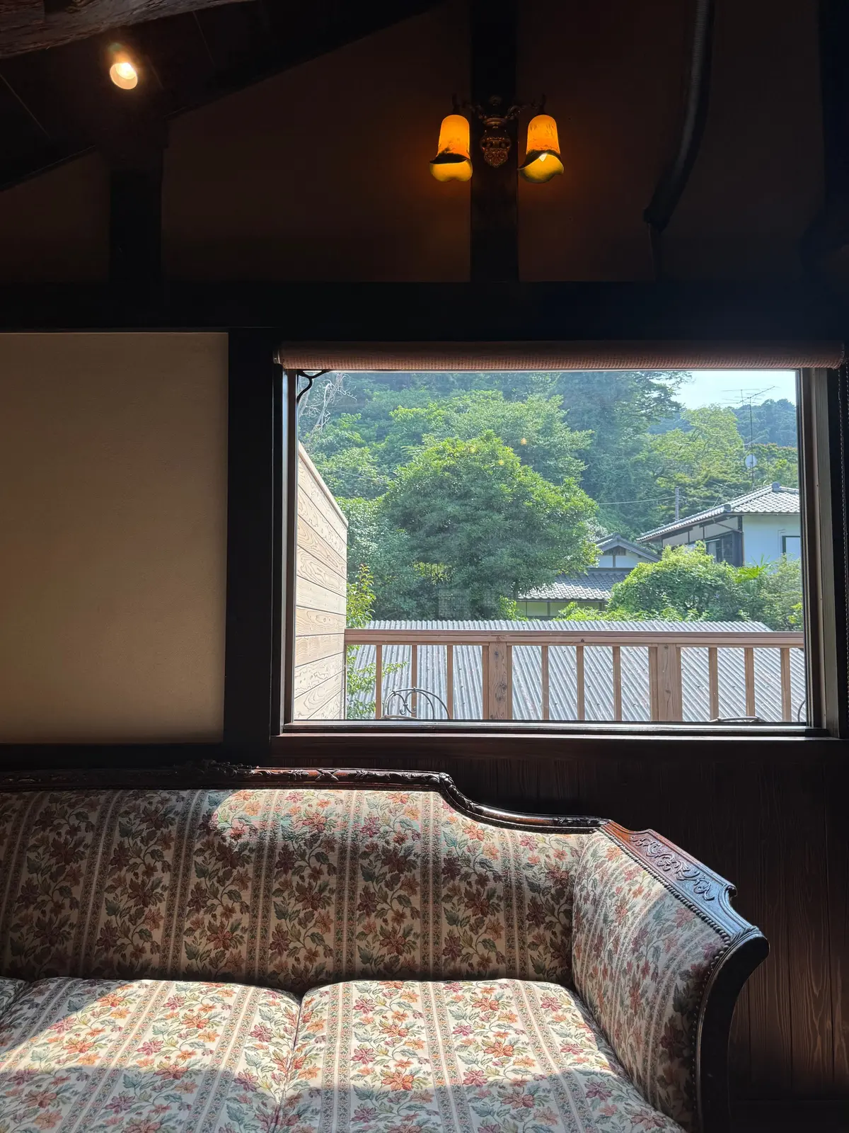 木造の梁がある部屋に、花柄のソファとテーブルが配置された休憩スペース。奥には山水の絵が描かれた障子が見える。女性が背後から見ている。