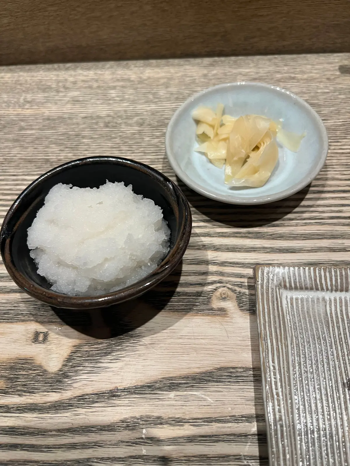 茶碗に白いシャリシャリとした雪のようなもの、青い小皿に薄黄色の柔らかい食べ物が置かれた木製のテーブル