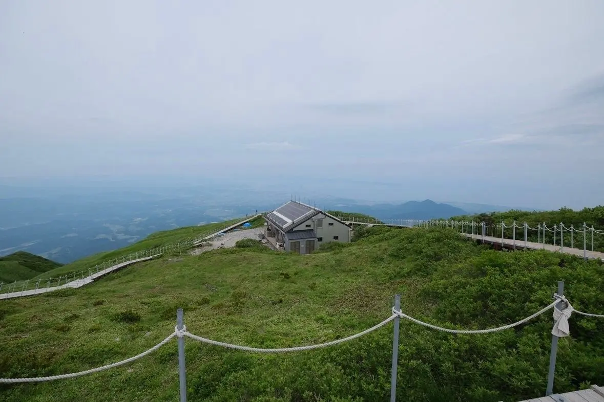 山頂に位置する建物と手すり付きの歩道、緑豊かな低木が広がる山頂の風景