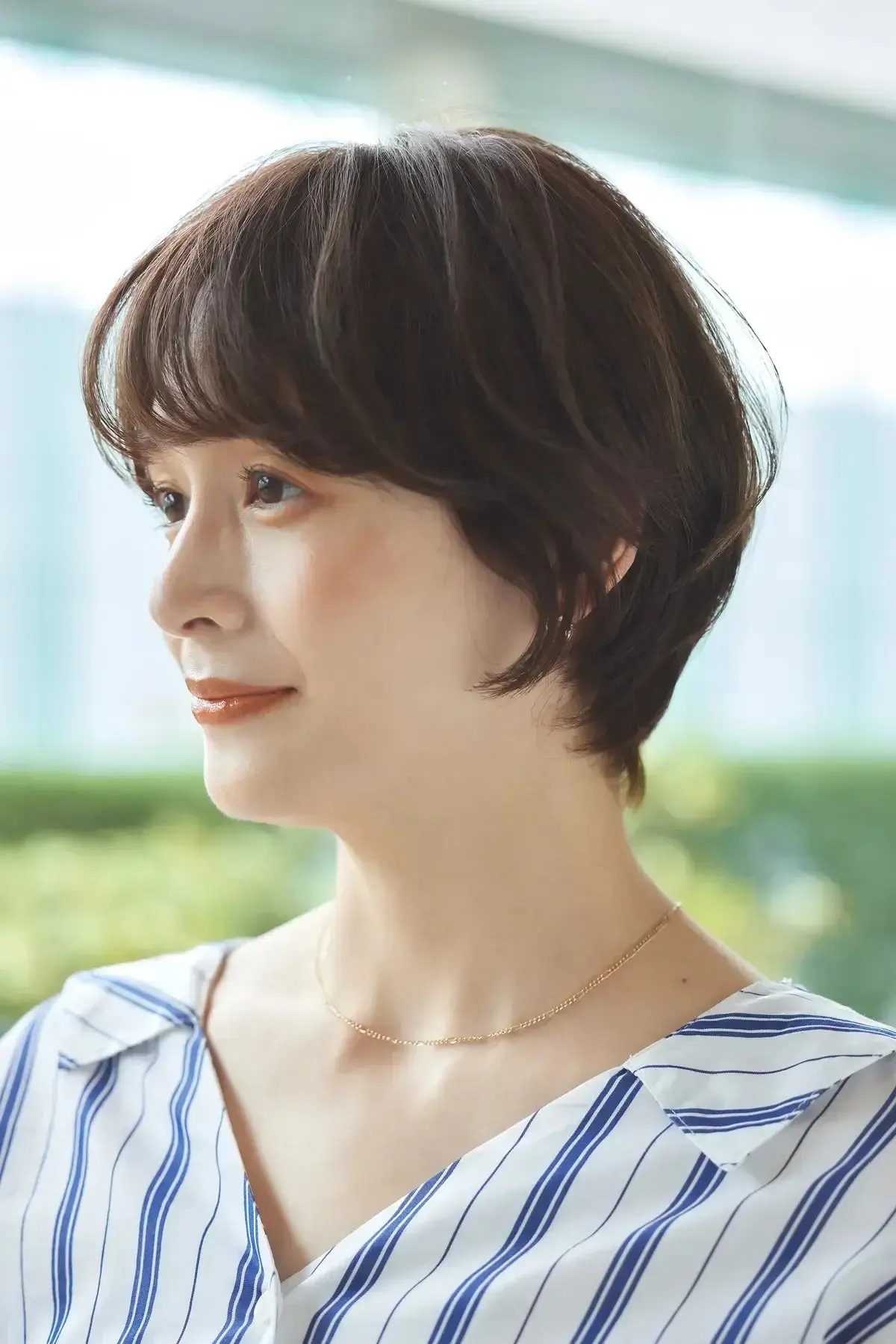 女性が白と青のストライプシャツを着て、短い黒髪で自然光の中を振り返っている。