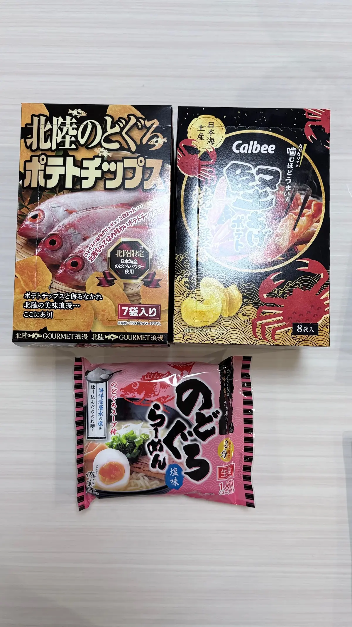 3種類の日本のスナック菓子。上から、北陸のどじょうポテトチップス（7袋入り）、カルビーの味付けホッケ（8袋入り）、そして「のりベエ」海苔風味スナック（1袋入り）。各パッケージには、商品の写真と日本語のテキストが記載されている。