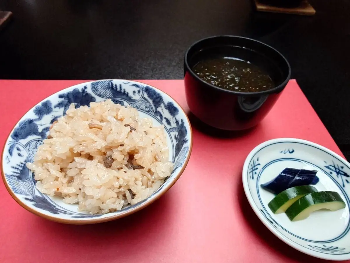 常磐ホテルの部屋食。ご飯、汁物、漬物のセット。ご飯は白地に青色の模様が入ったお皿に盛り付けられ、汁物は黒いどんぶり、漬物は小さな白磁のお皿に入っている。