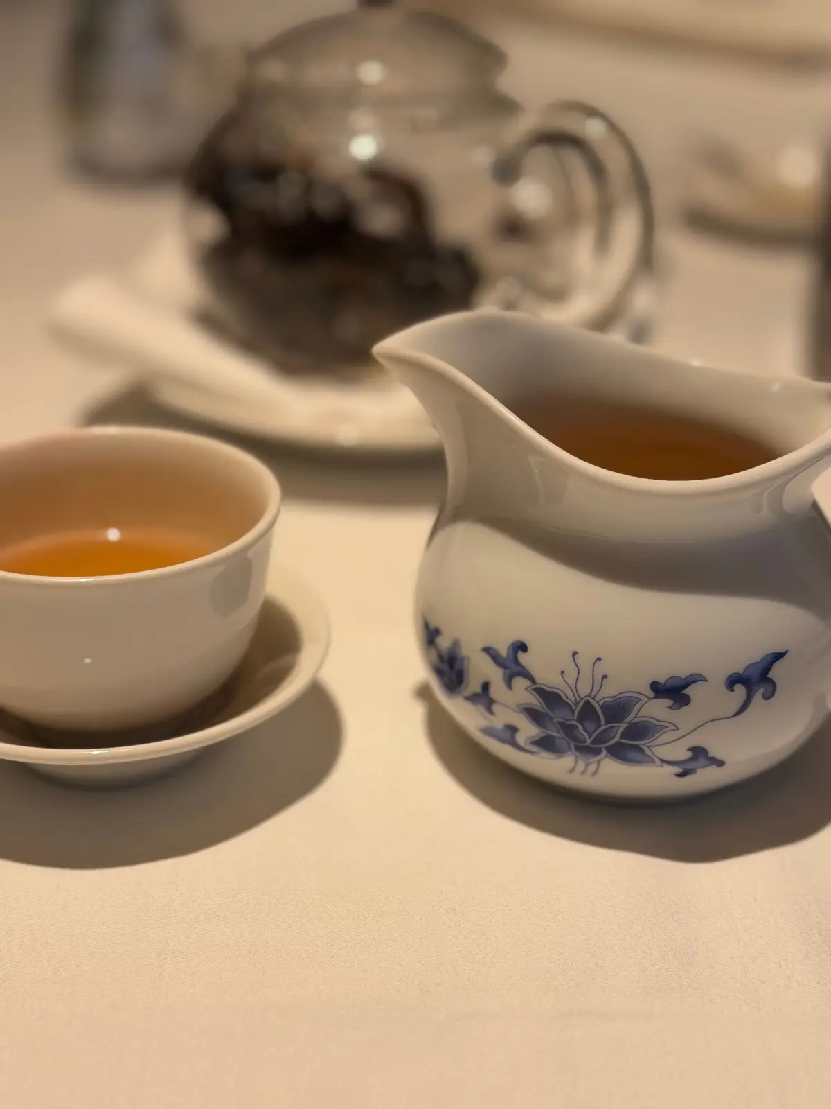 白いカップに茶色いお茶と青い花模様のピッチャーが置かれたテーブル