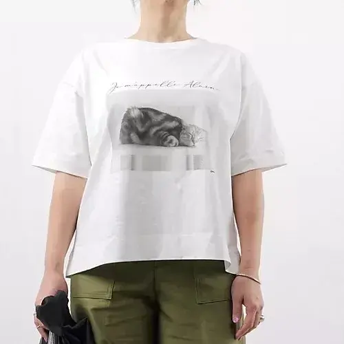 白のオーバーサイズTシャツに、横たわる猫のモノクロ写真と「Jumapple Alain」の文字がプリントされている。猫はテーブルの上に寝そべり、リラックスした様子。Tシャツはゆったりとしたシルエット。