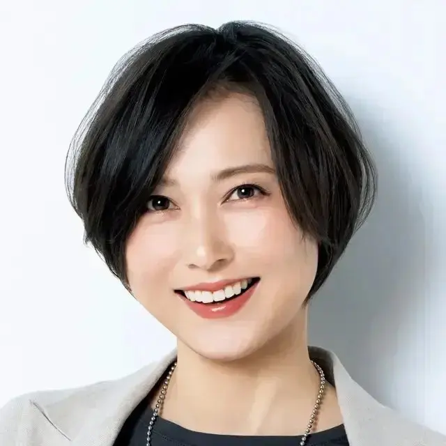 黒いショートヘアの女性が淡い色のブレザーを着て、真ん中を向いて微笑んでいる