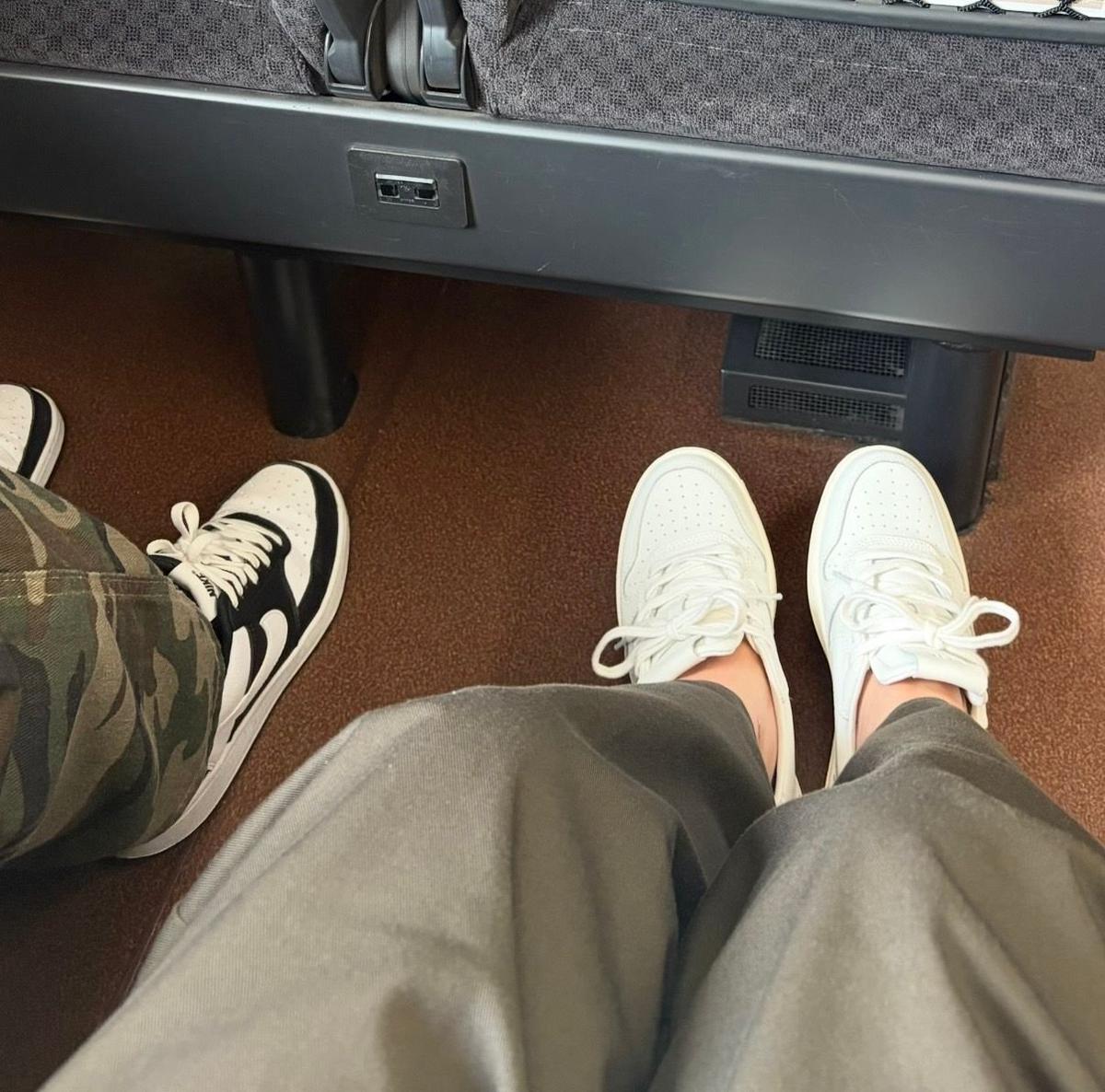新幹線の座席に2人で並んで座っている足元。右側にカーキ色のズボン、白いスニーカーを履いている人が座り、左側に迷彩柄のズボン、黒と白のNikeのスニーカーを履いている人が座っている。