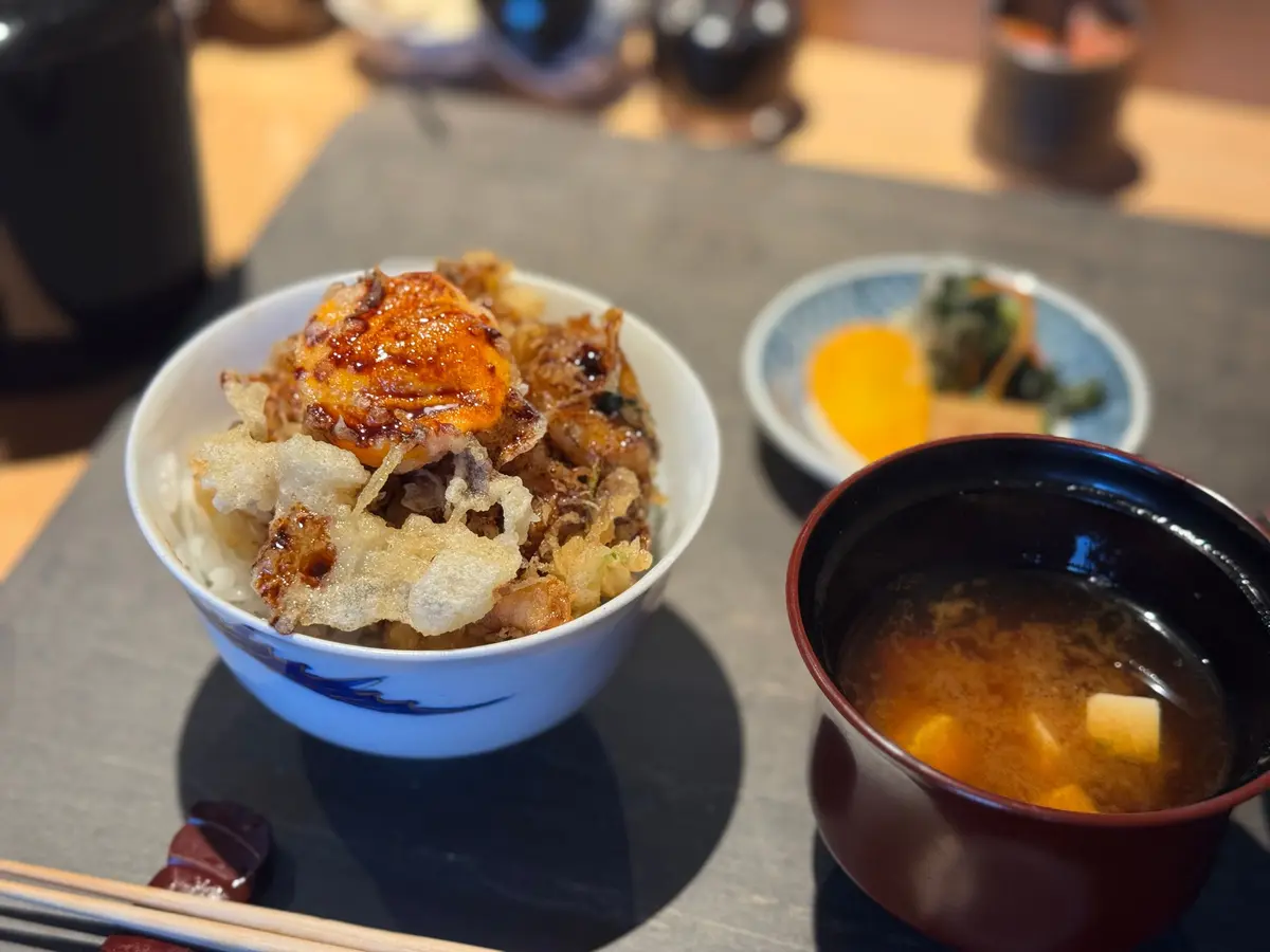 白米の上に天ぷらを盛り付けた丼、小鉢に入った黄色い柑橘類、漆器の味噌汁椀が置かれた食卓。
