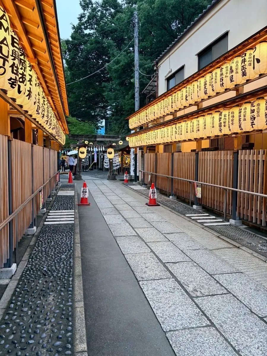 両側に木造の建物が並ぶ石畳の道で、建物には多数の提灯が吊るされ、中央に鳥居が設置されている。