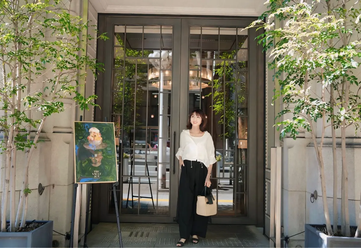 金色の縁取りの立て看板に、氷菓「THE VAULT ICE」のメニューが掲示されている。氷菓は器に盛り付けられ、フルーツやクリームが添えられている。背景には建物の入り口が見える。