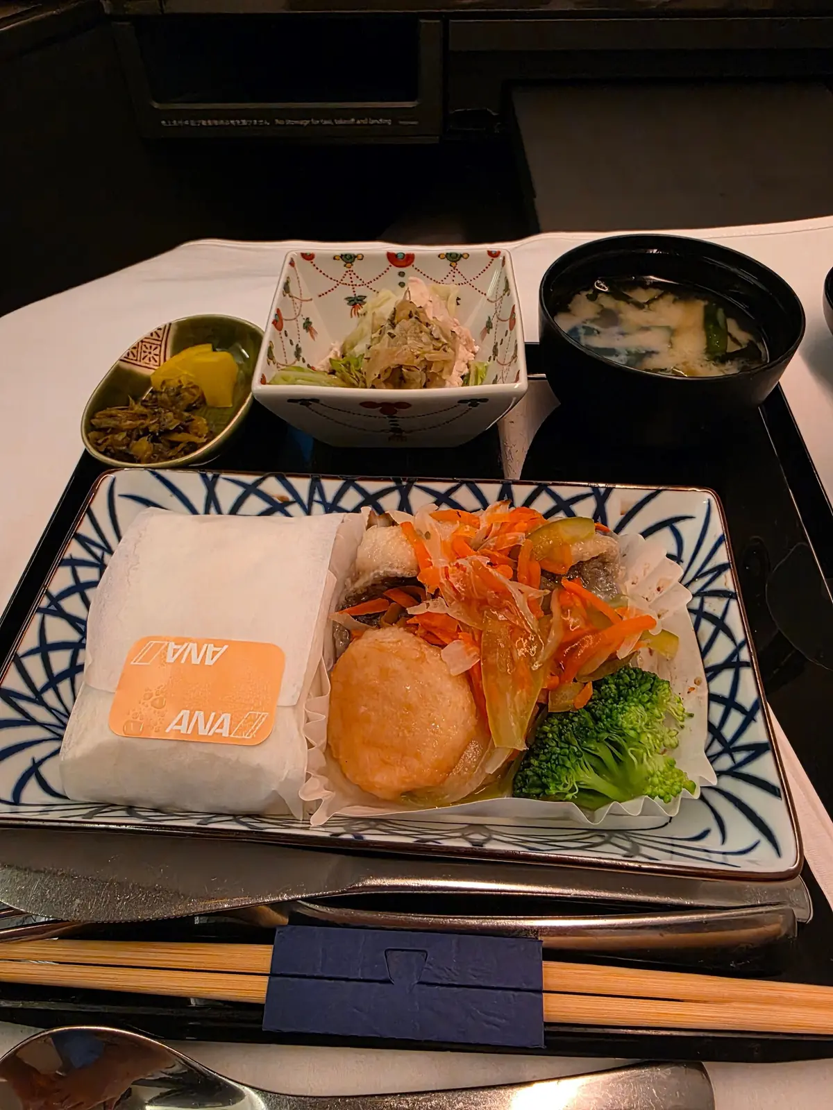 ANA機内食の和食。ご飯に焼き魚、野菜の煮物、お吸い物、漬物がセット。白いテーブルクロスに置かれたトレイに入っている。