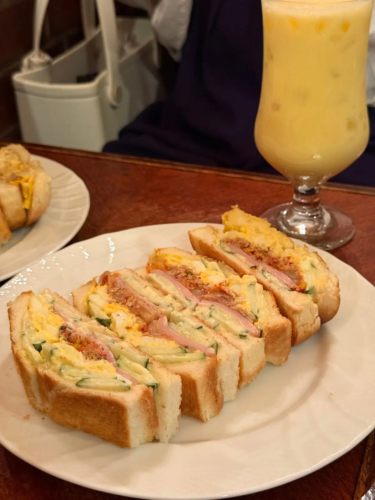 サンドイッチと卵料理が並んだ白い皿と、黄色のジュースがグラスに入ったカフェのテーブル