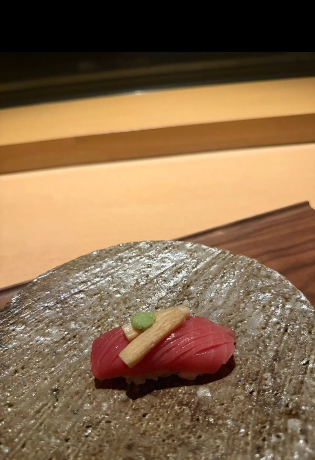 握り寿司。赤身のマグロが乗っており、上に木の芽と和風の飾り切りが添えられている。表面が粗い石の皿の上にある。